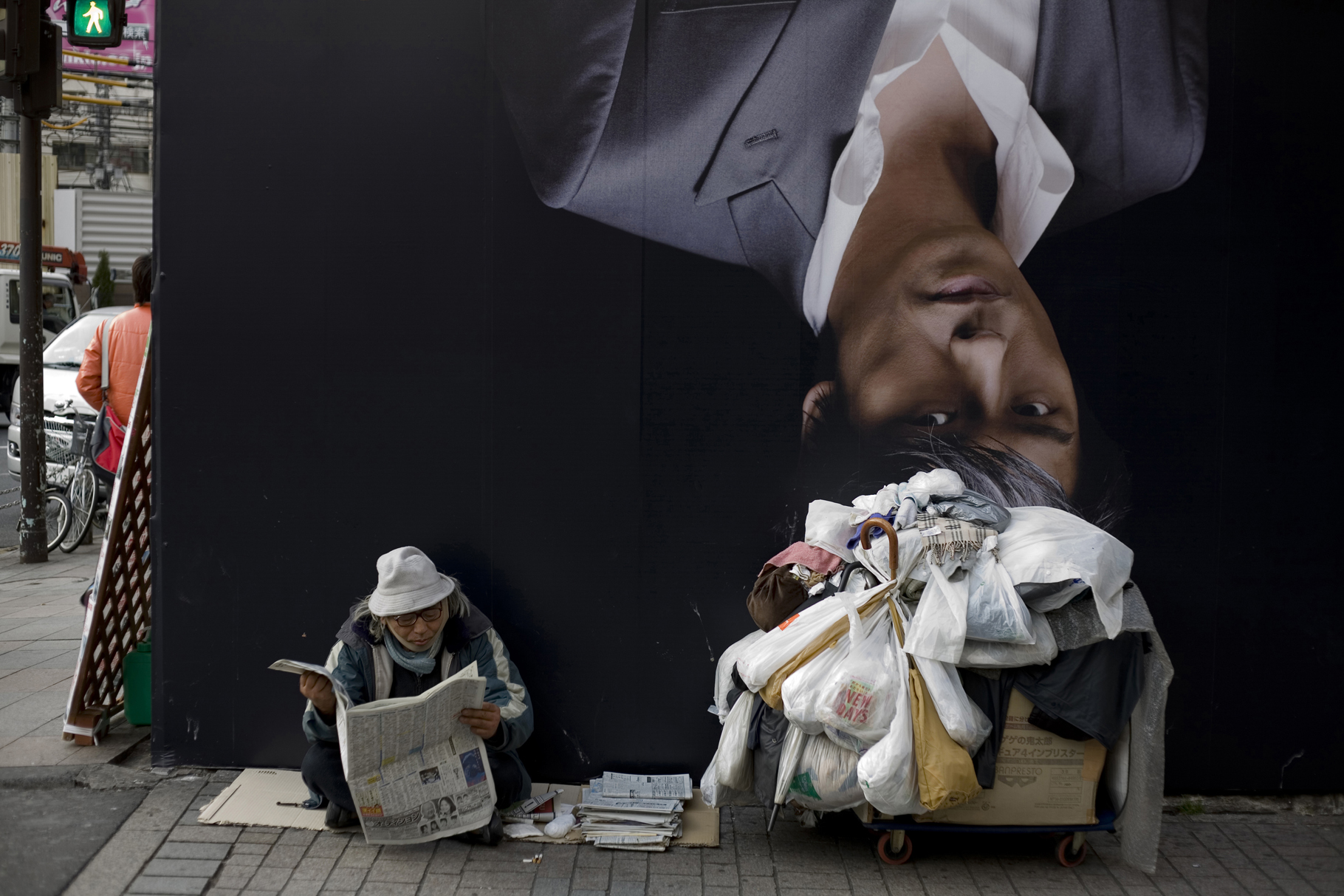 Un SDF lit son journal dans le quartier du Kabuki-cho devant une affiche de publicité.